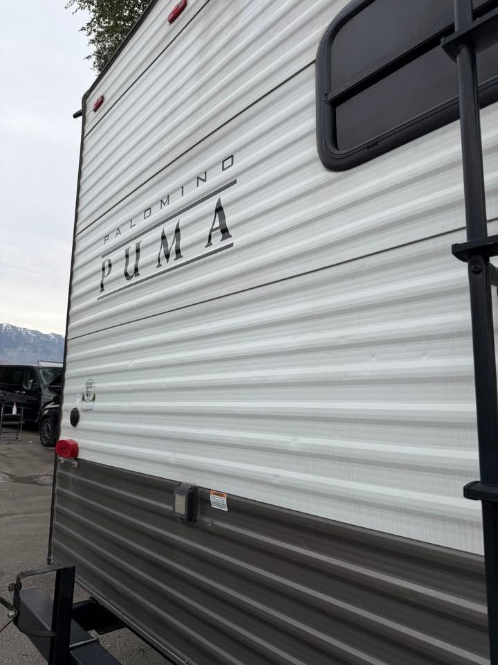 Side view of a Puma travel trailer with a black ladder, window, and the brand name displayed.