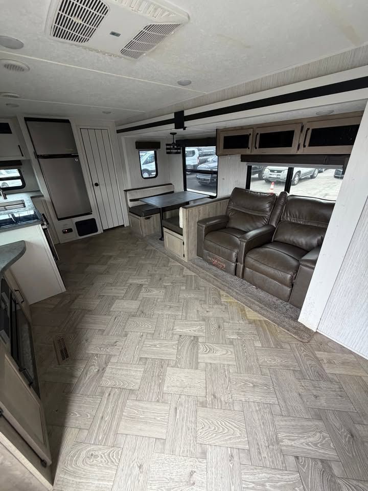 Interior of a recreational vehicle. Features include a table, chairs, sofa, and kitchen appliances.