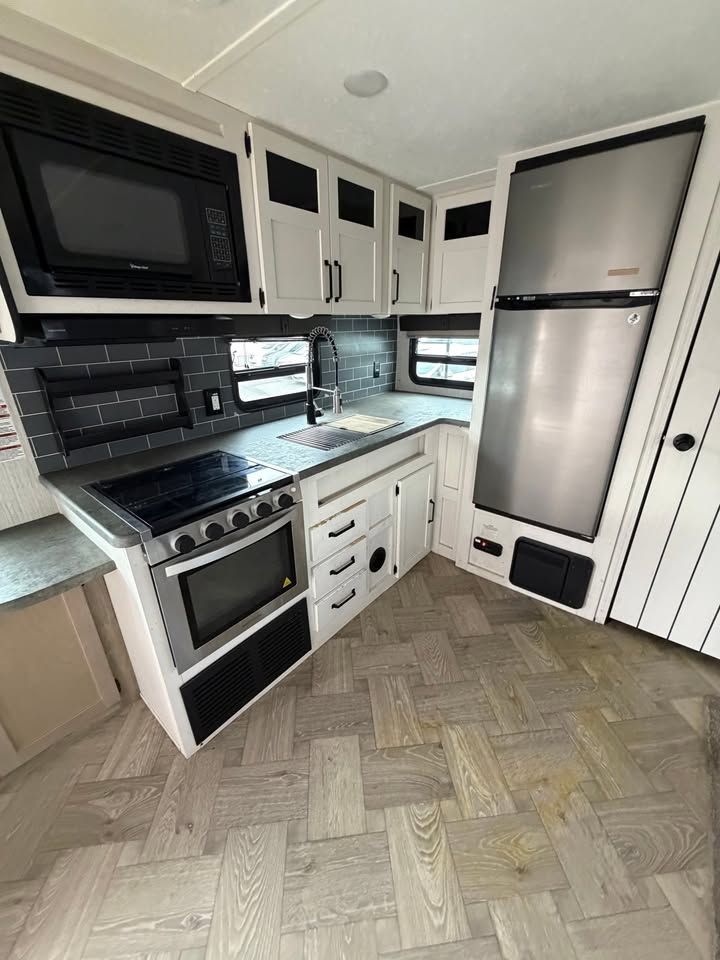 RV kitchen with a microwave, stove, cabinets, refrigerator, and patterned floor.