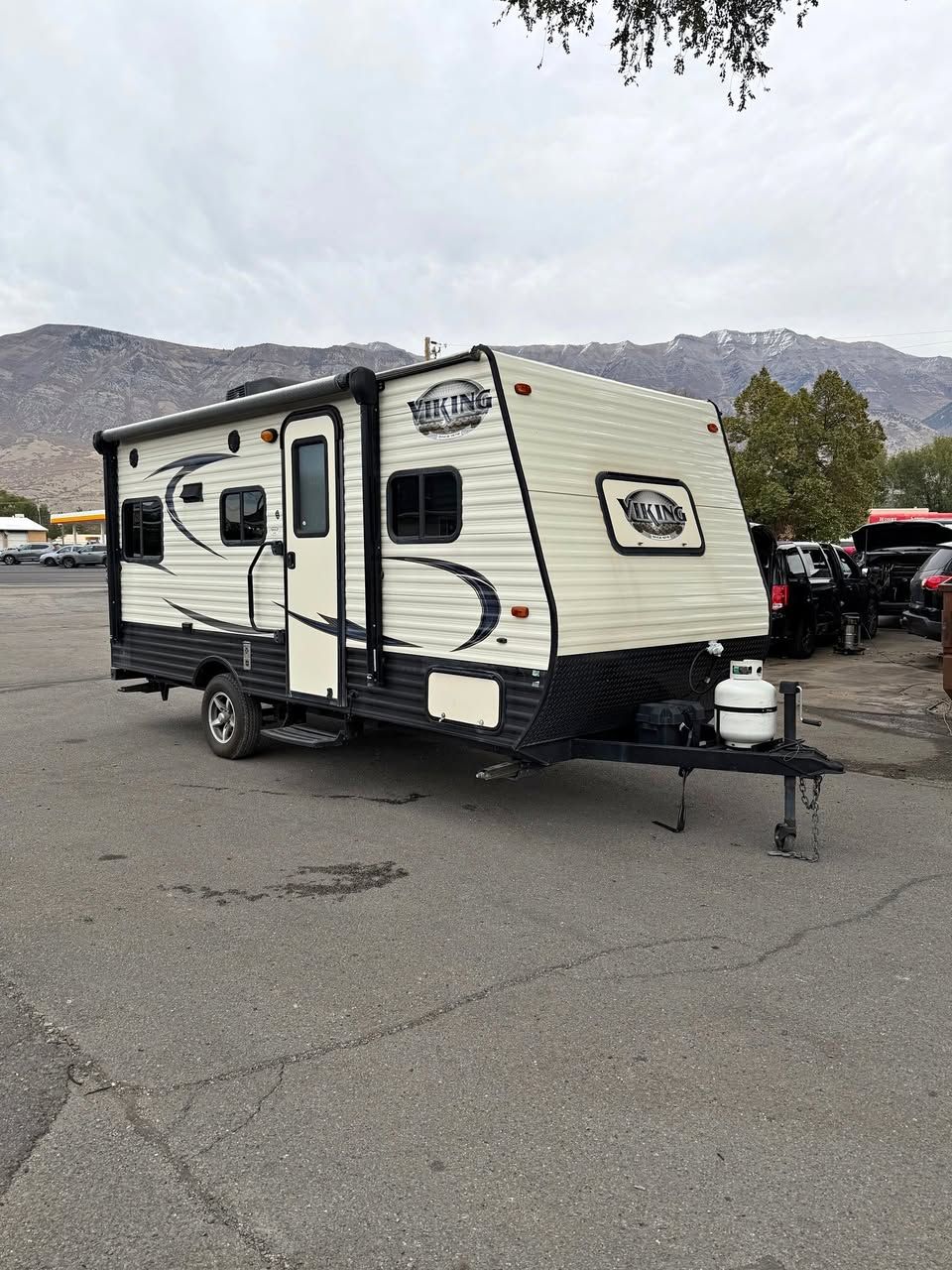 Cream and black travel trailer parked on asphalt.  Mountains in the background under cloudy sky.