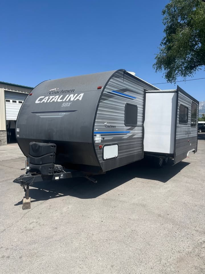 Gray and blue Catalina travel trailer with slide-out in a paved lot on a sunny day.