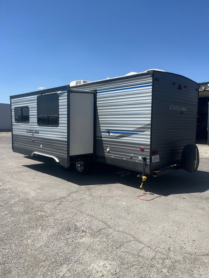Gray and blue travel trailer with open door parked on concrete.