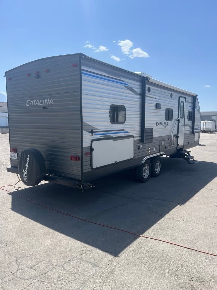 Gray and blue travel trailer with spare tire, parked on asphalt.