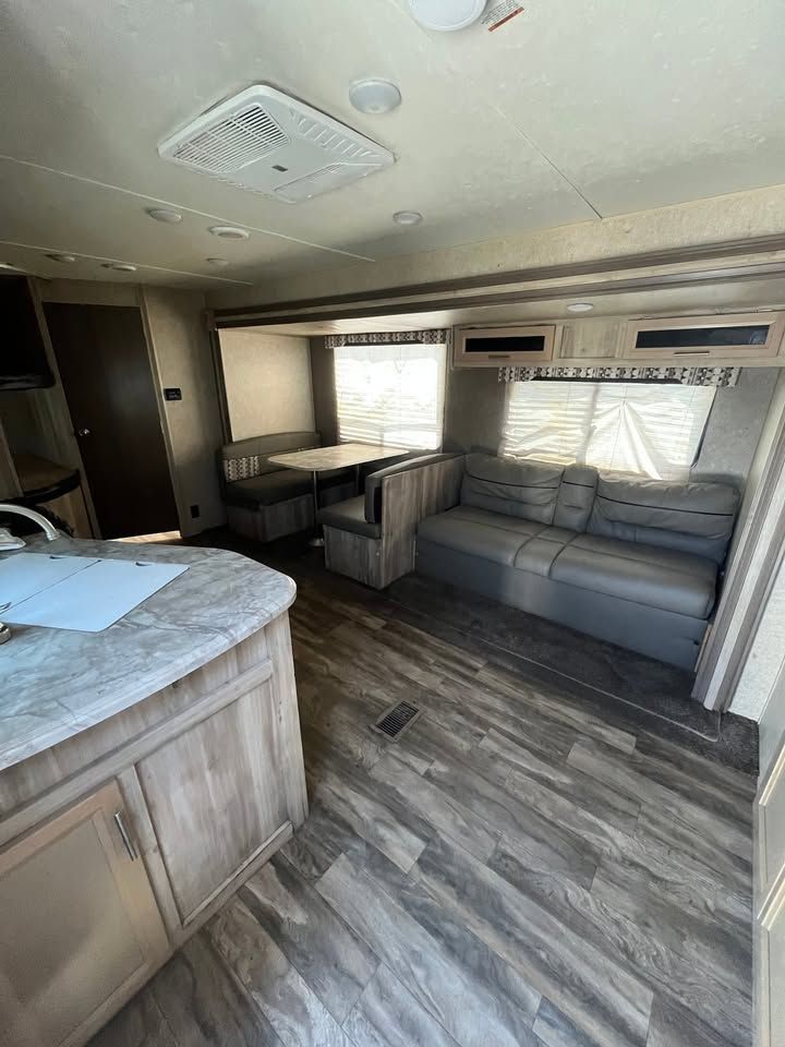 RV interior with a kitchen counter, dining area, and sofa. Wood-look flooring, light gray walls.