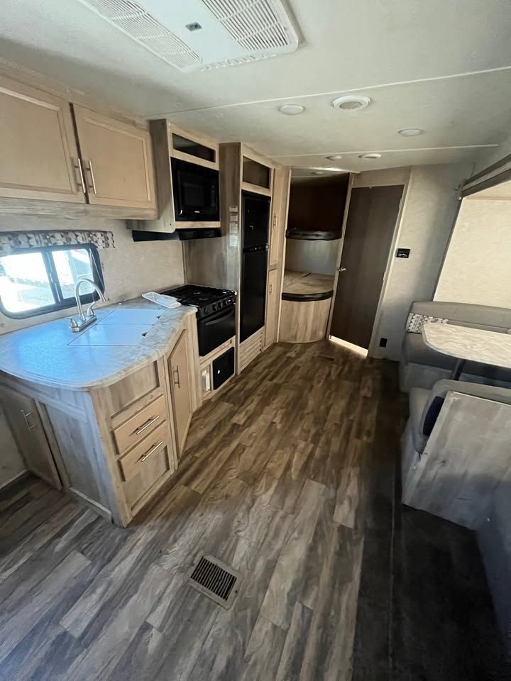 Interior of a camper. Kitchen with countertops, appliances, and dining area with booth seating, wood-like flooring, and cabinets.