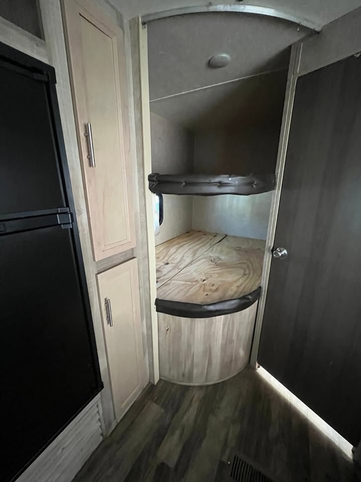 Interior of a camper featuring bunk beds, cabinets, a refrigerator, and wood-look flooring.
