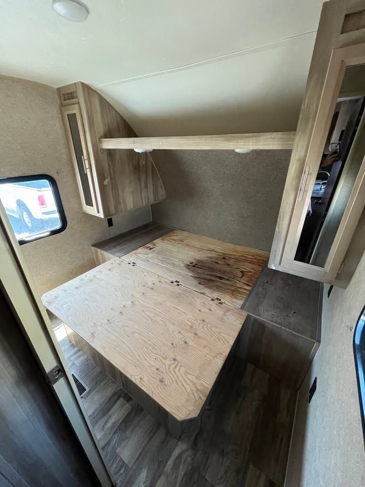 Interior of RV with a bed, cabinets, and a table.