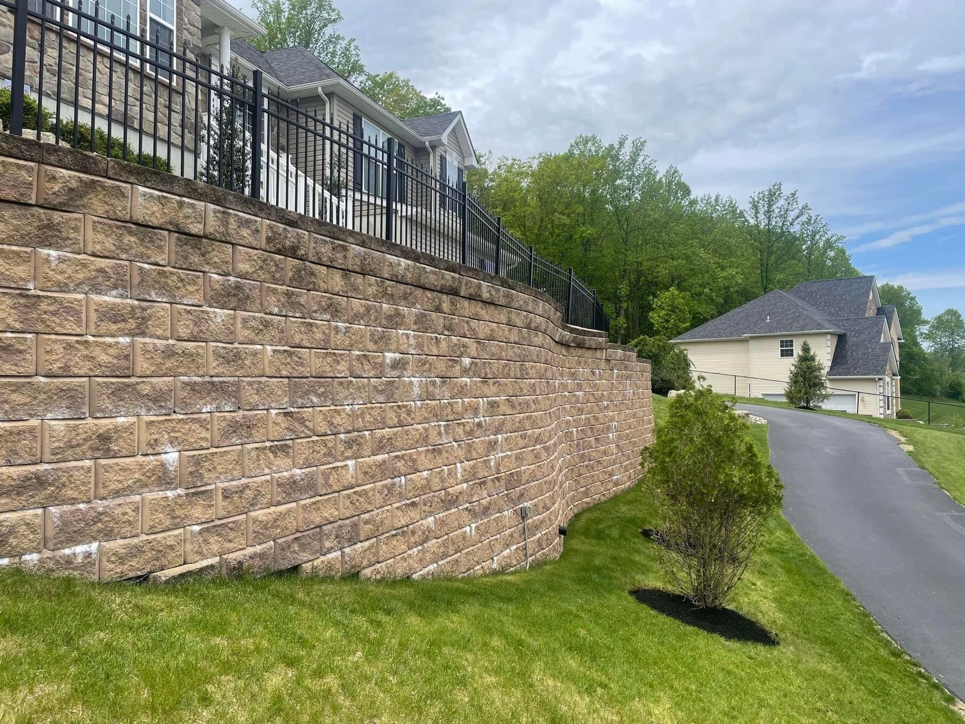 a large brick wall surrounds a driveway leading to a house .