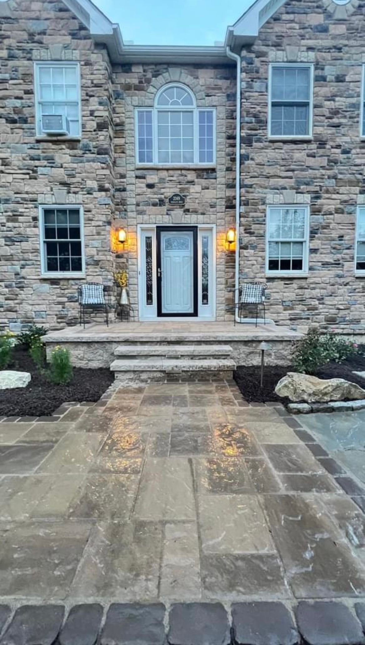 A large stone house with a brick walkway leading to the front door.