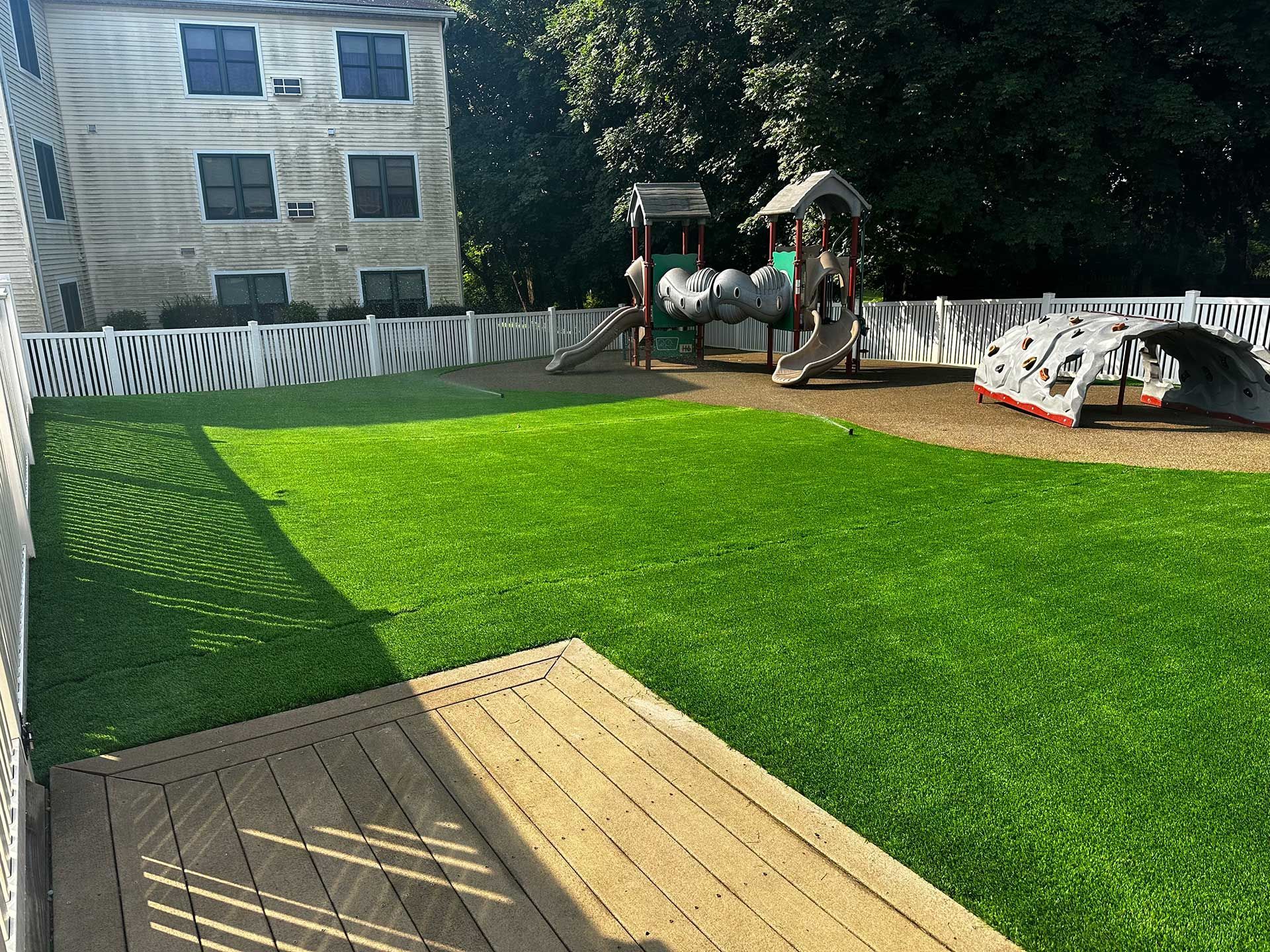 A backyard with synthetic turf, a playground, and  a wooden deck