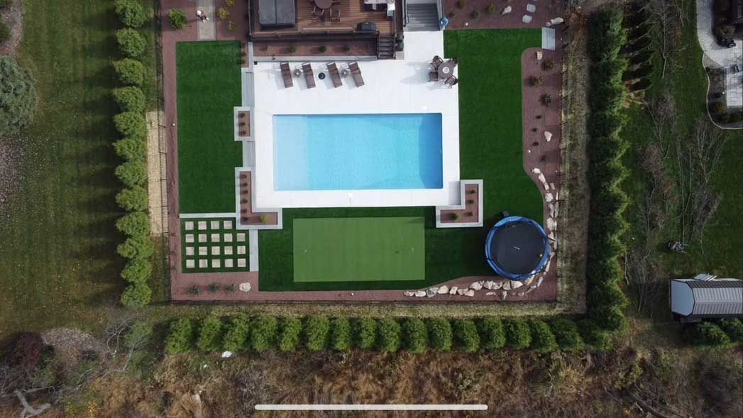 An aerial view of a large backyard with a swimming pool and artificial grass around it