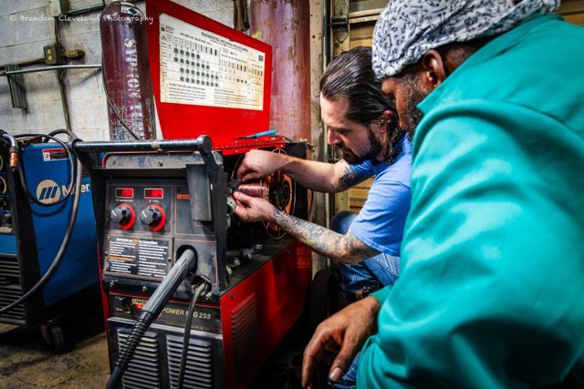Two workers adjust a red welding machine in an industrial workshop