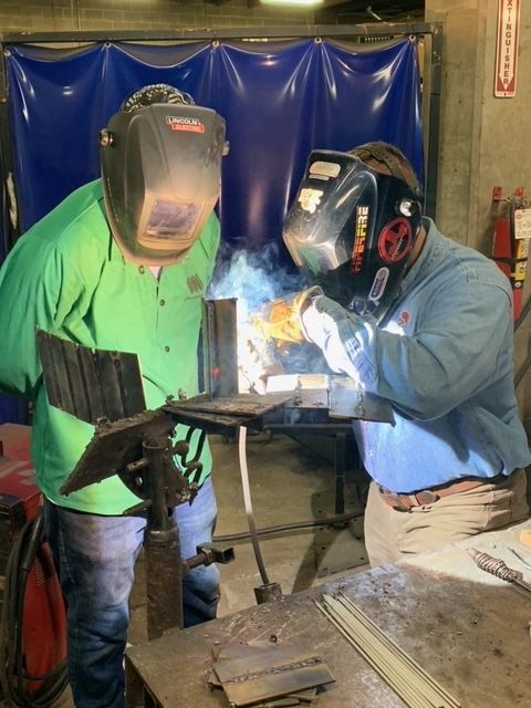 Student welding while a teacher is watching