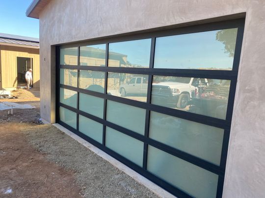 Garage door with black framing and frosted glass panels, reflecting a white truck.