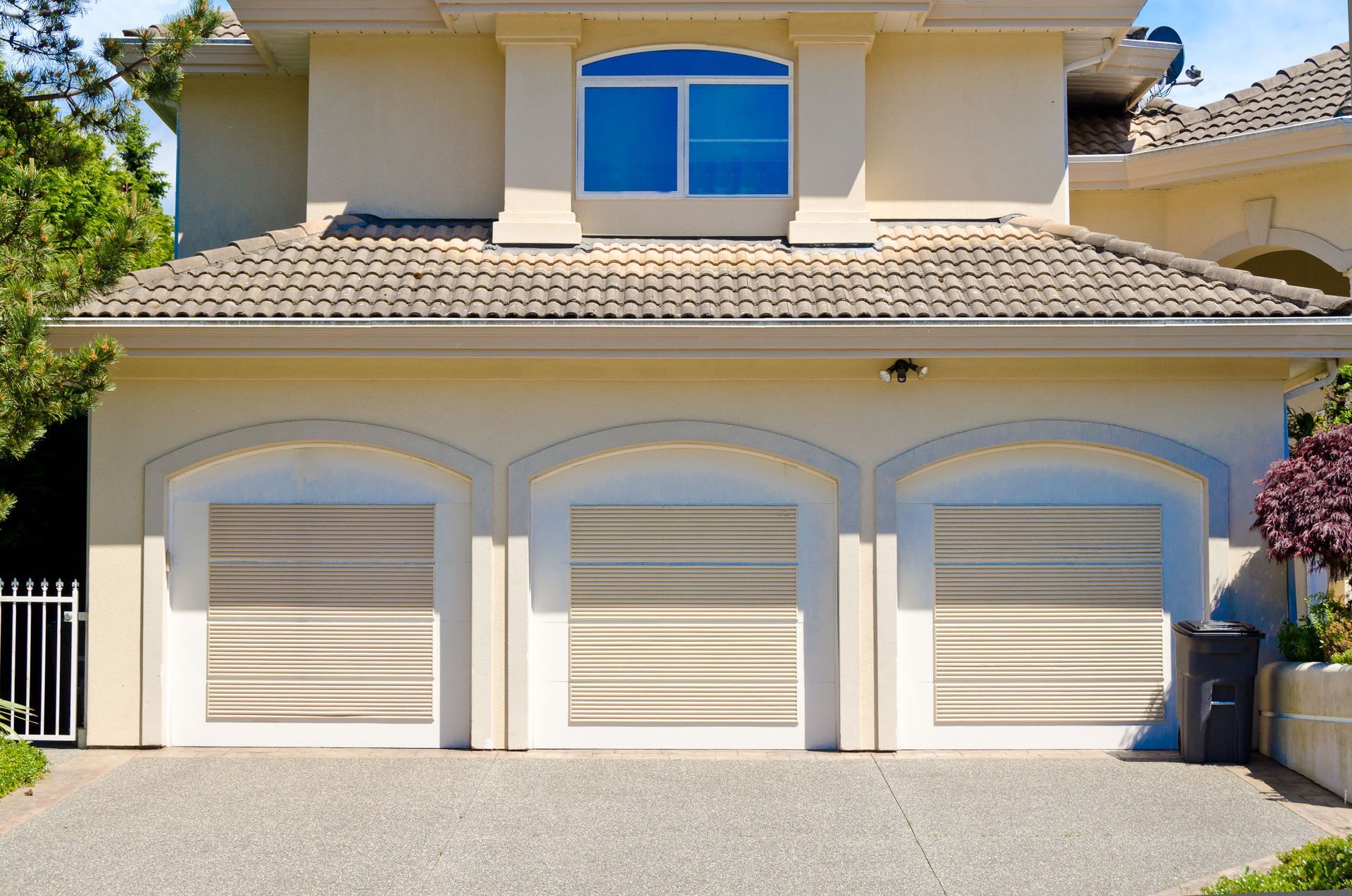 Tan three-car garage with roller doors, beige stucco, and a blue window above.