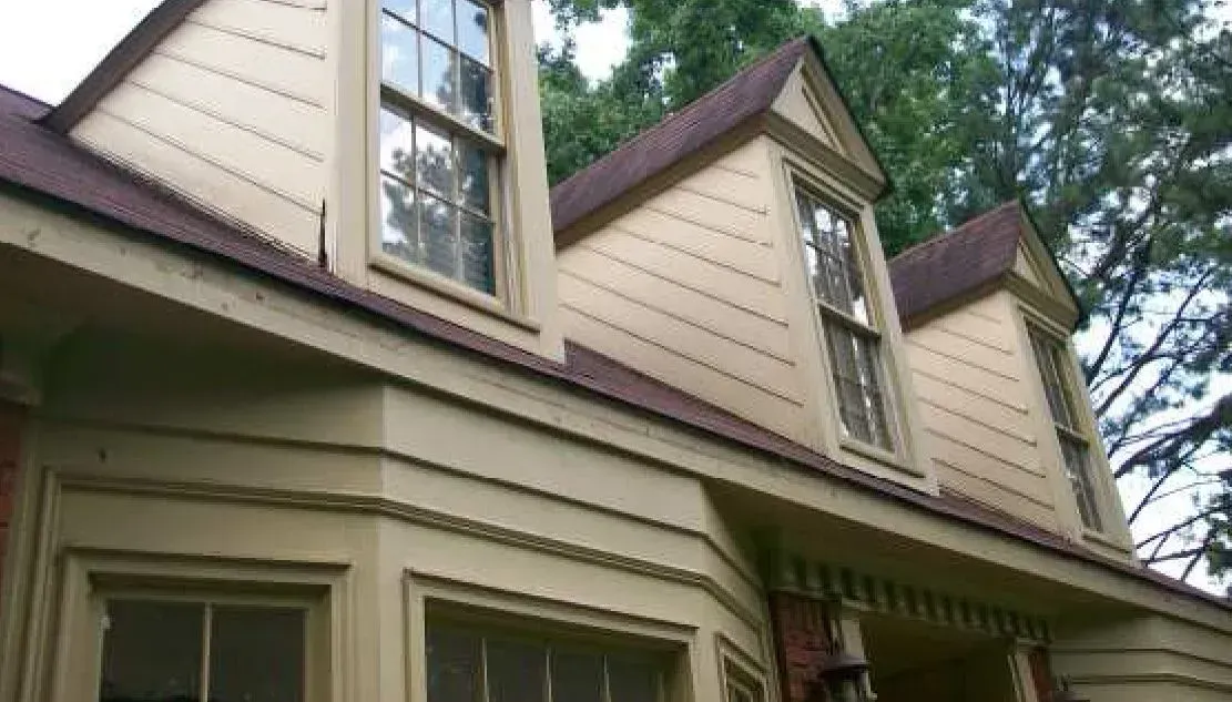 Yellow house with brown roof and three dormer windows.