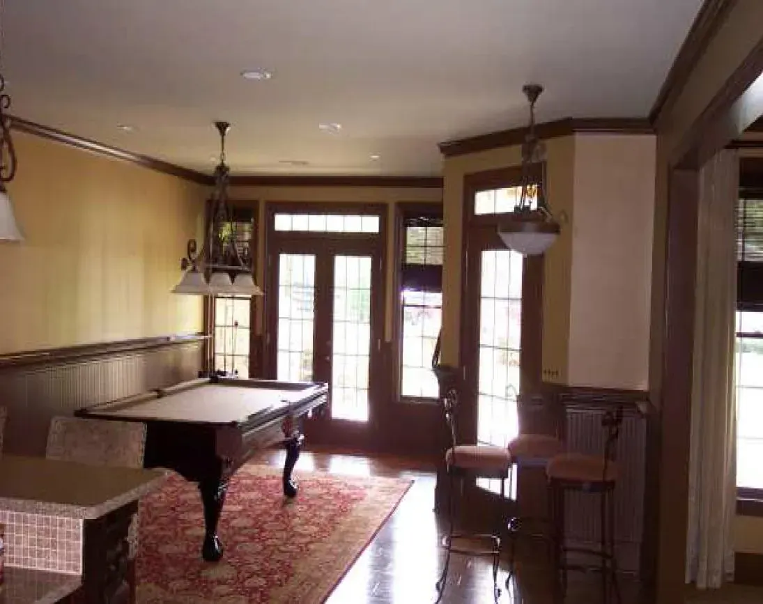 Pool table in a room with wood trim and double doors. A patterned rug and pendant lights are visible.