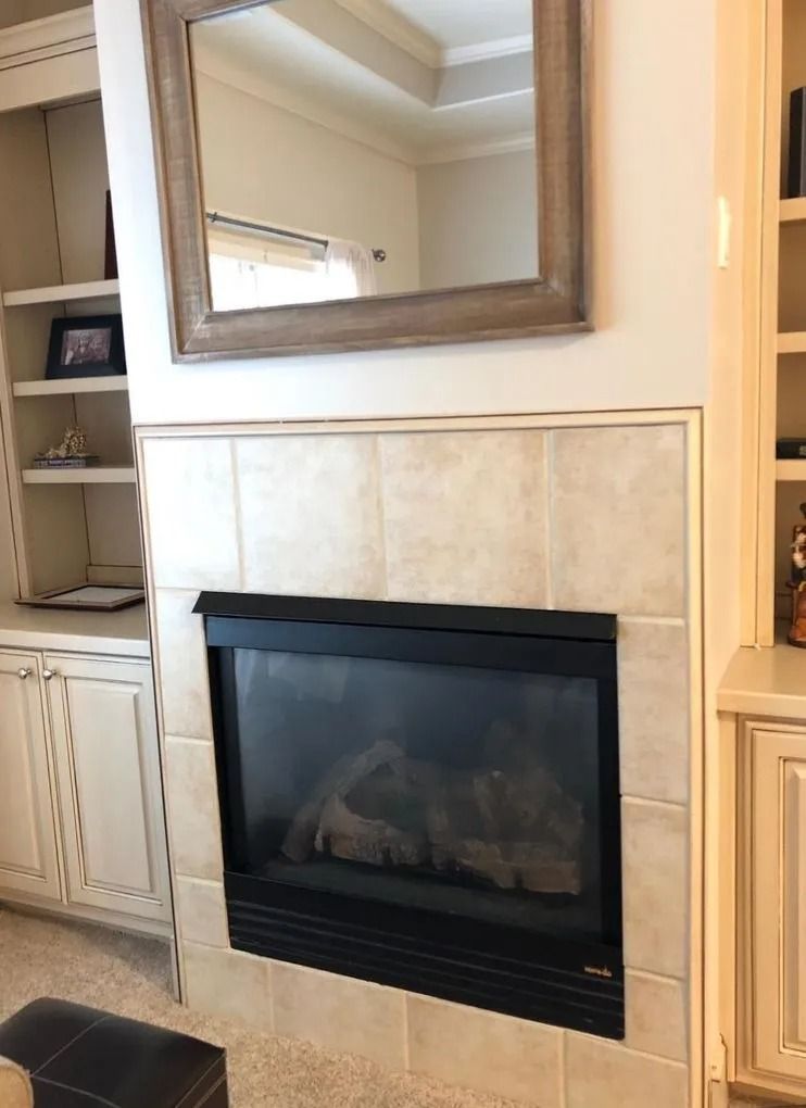 Fireplace with black surround, beige tiled surround, mirror above, and built-in shelving.