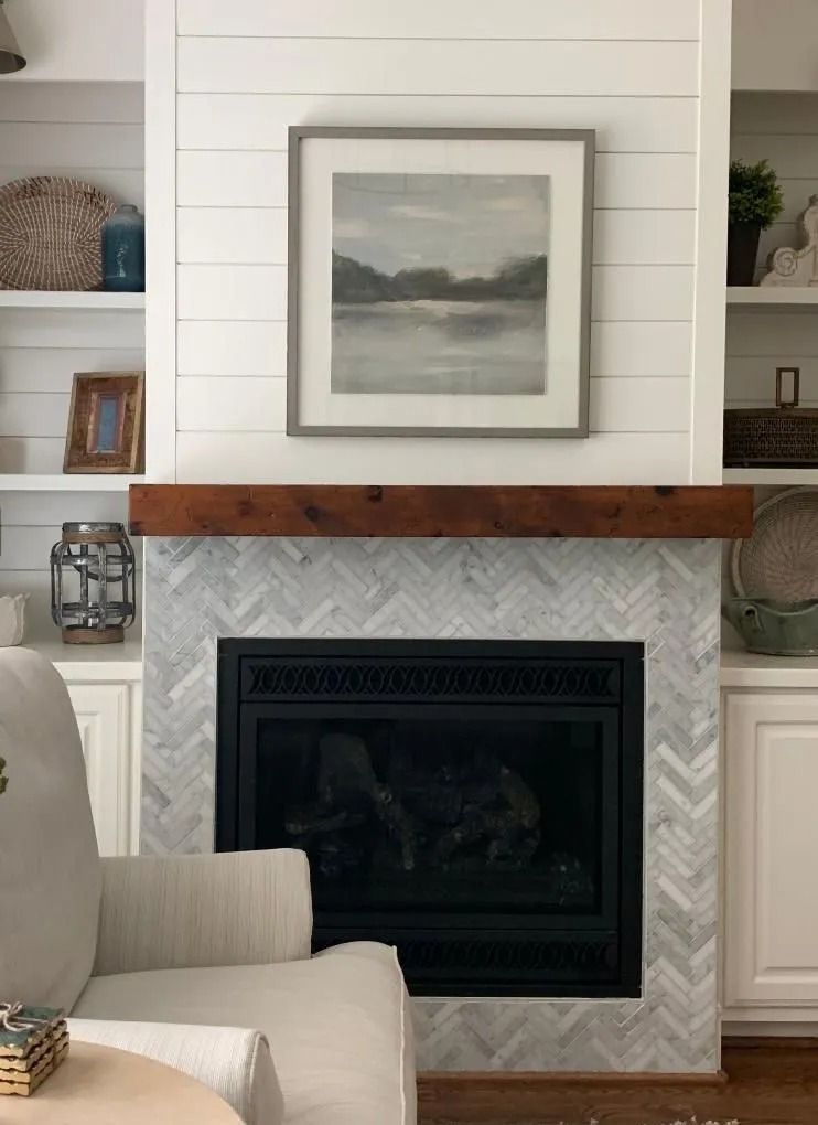 Fireplace with marble herringbone tile, wooden mantel, and artwork above. Built-in white shelves on either side.
