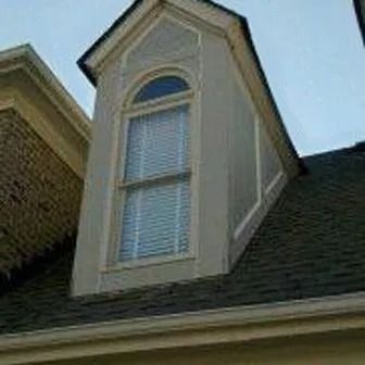 Dormer window with arched top, light gray siding, white trim, and a window with blinds on a dark roof.