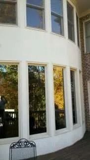 White stucco house with tall windows reflecting trees and a black wrought iron chair.