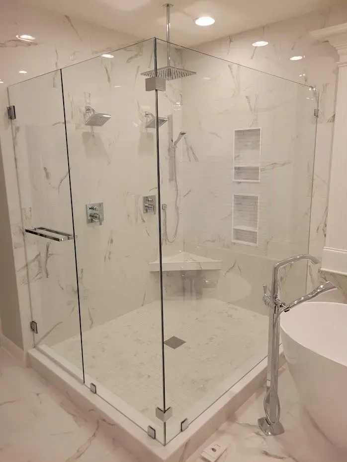 Corner glass shower with white marble tile, chrome fixtures, and built-in bench.