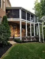 Two-story screened porch with white columns, black railings, and green lawn.