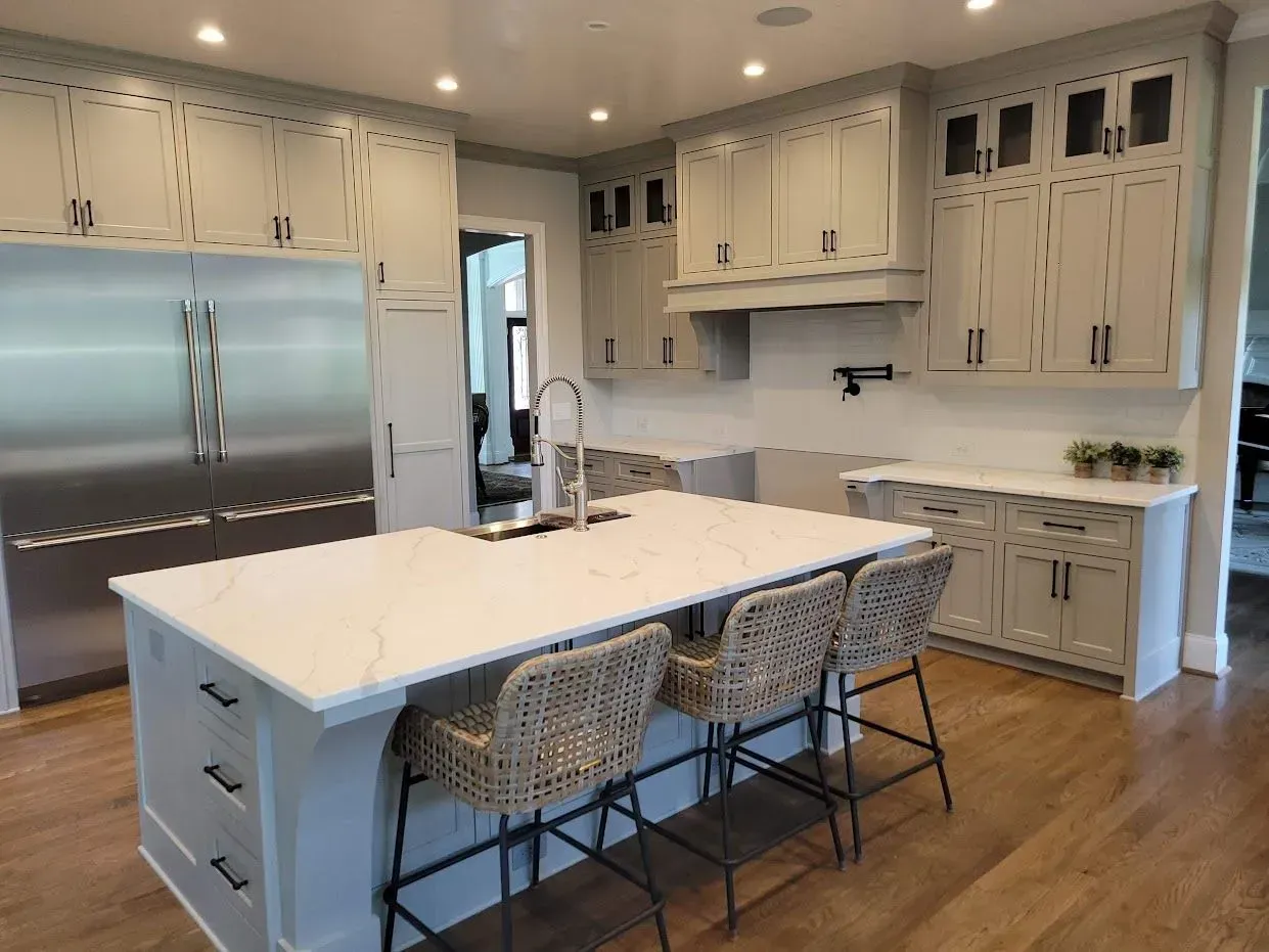 Modern kitchen with gray cabinets, white island with stools, stainless steel refrigerator.