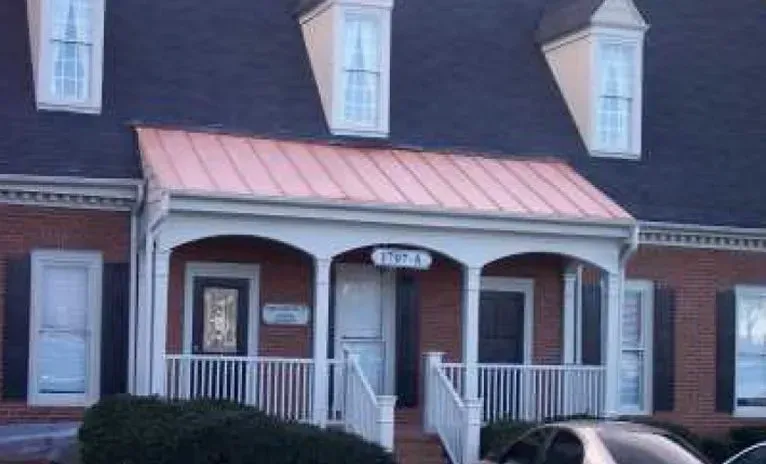 Red brick building with a copper-roofed porch. White railing, black shutters, and dormer windows above.
