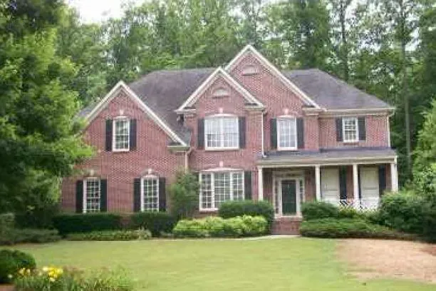 Two-story brick house with black shutters and a green lawn.