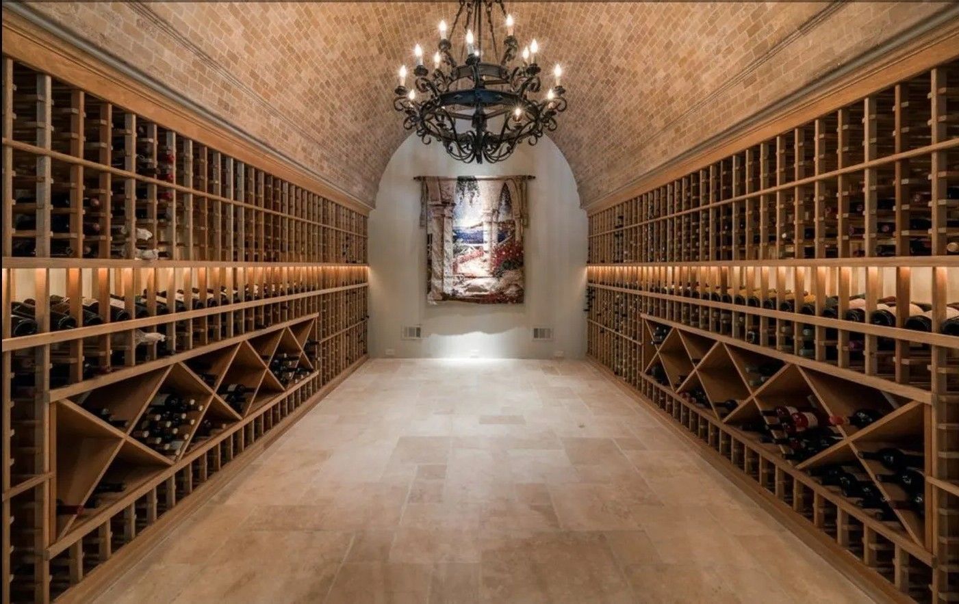 Wine cellar with arched brick ceiling, filled with wooden racks of wine bottles, and a chandelier.