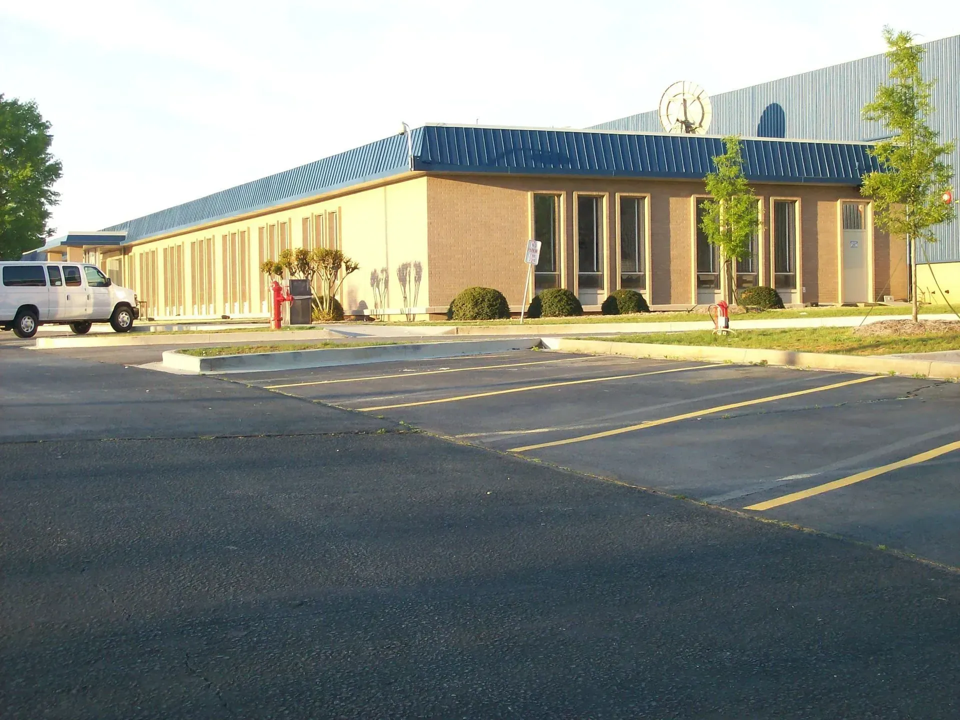 Tan building with blue roof; white van parked in front, parking lot in foreground.