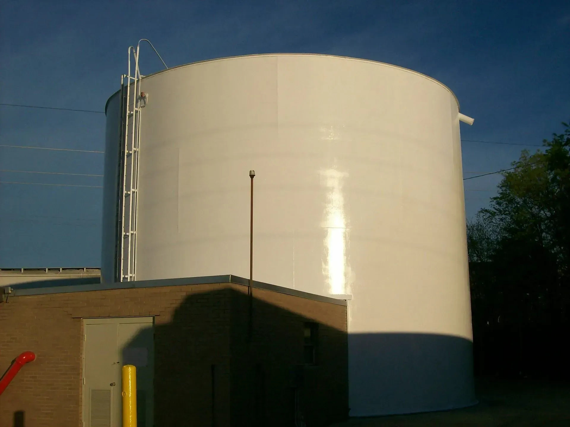 Large white cylindrical water tank next to a brown brick building, with a ladder on its side.