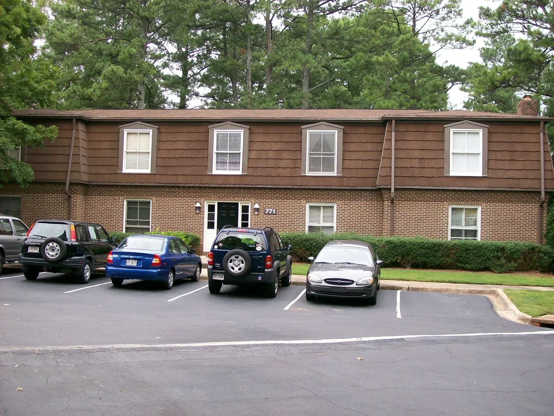 Two-story brown brick building with multiple windows and parked cars in a parking lot.