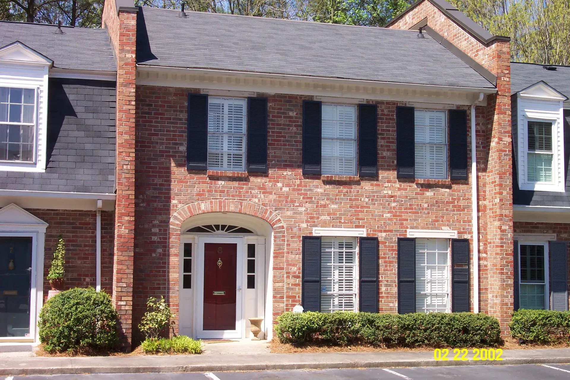 Brick townhouse with black shutters, red front door, and grey roof.