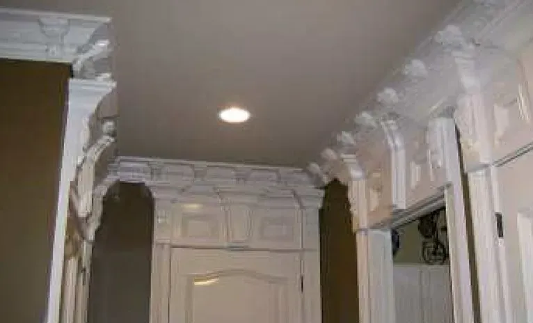 Ornate white crown molding above a white door, with a recessed ceiling light.