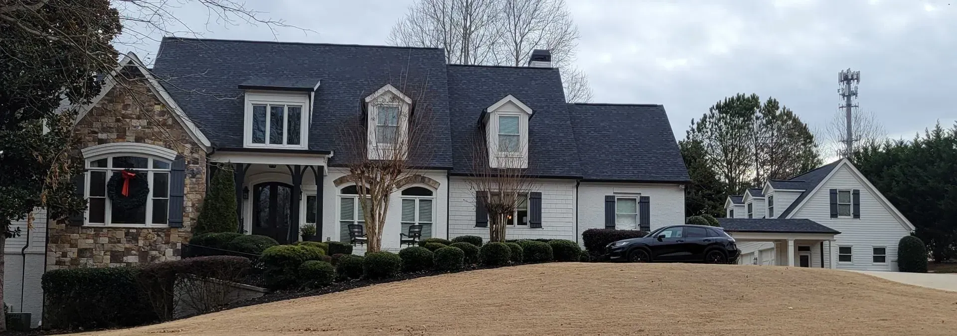 A large house with a stone facade and black car in front, under a cloudy sky.