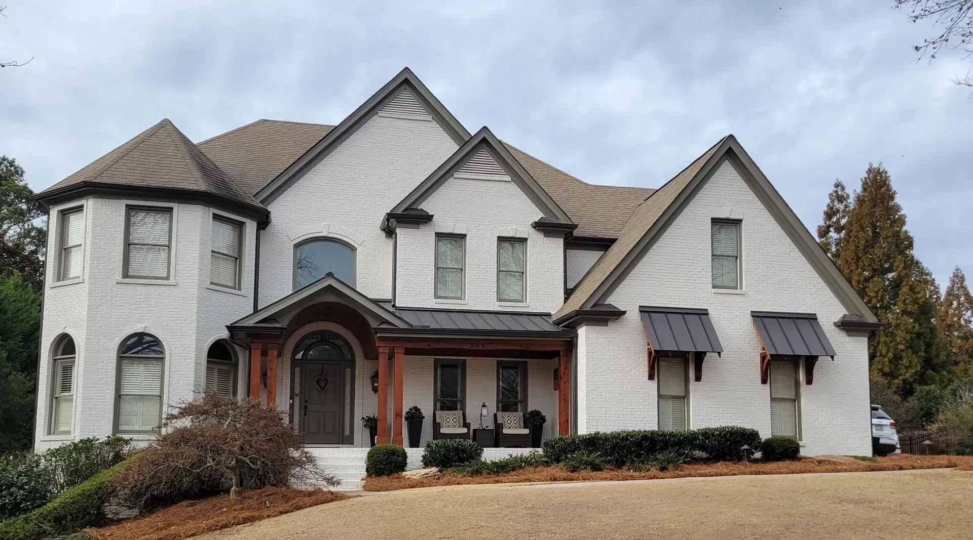 White brick house with multiple roof gables, a turret, and a covered porch. Overcast day.