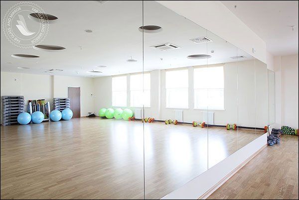 Empty gym with mirrors, exercise balls, weights, and step platforms. Bright room with wooden floor.