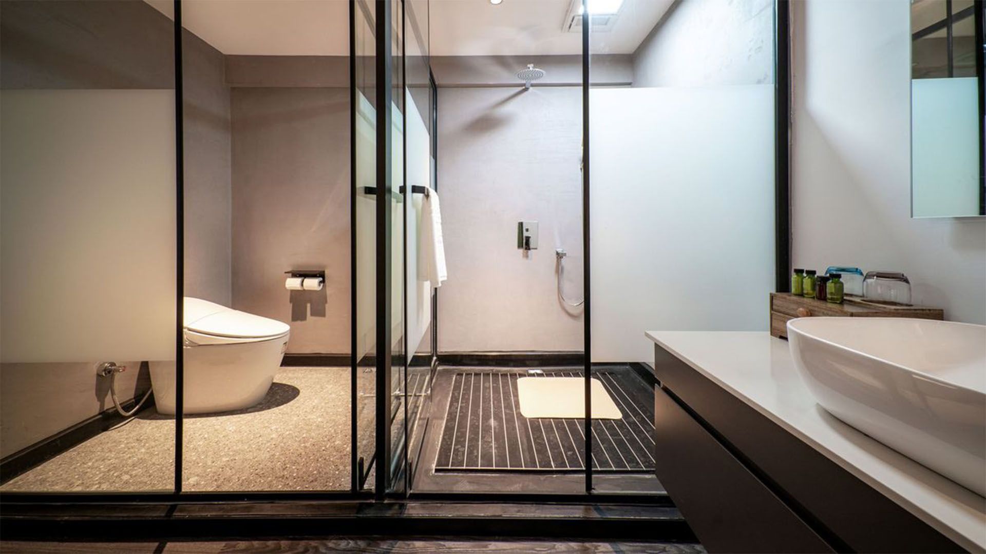 Modern bathroom with glass shower, white toilet, and floating sink. Gray walls.