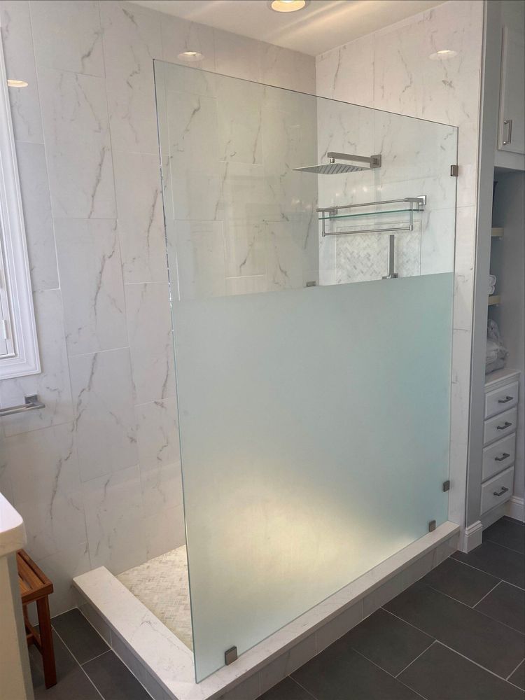 Modern shower with partial frosted glass screen, white marble tile, and chrome fixtures.