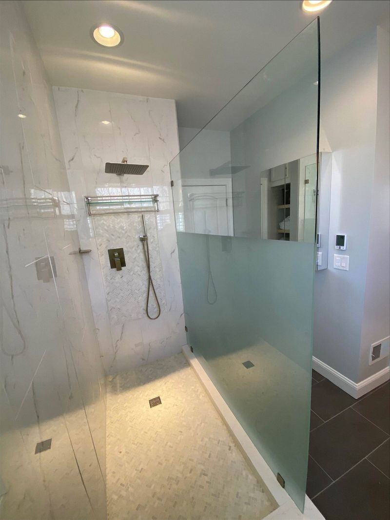 Modern shower with marble tile, glass enclosure, and dark floor tiles.