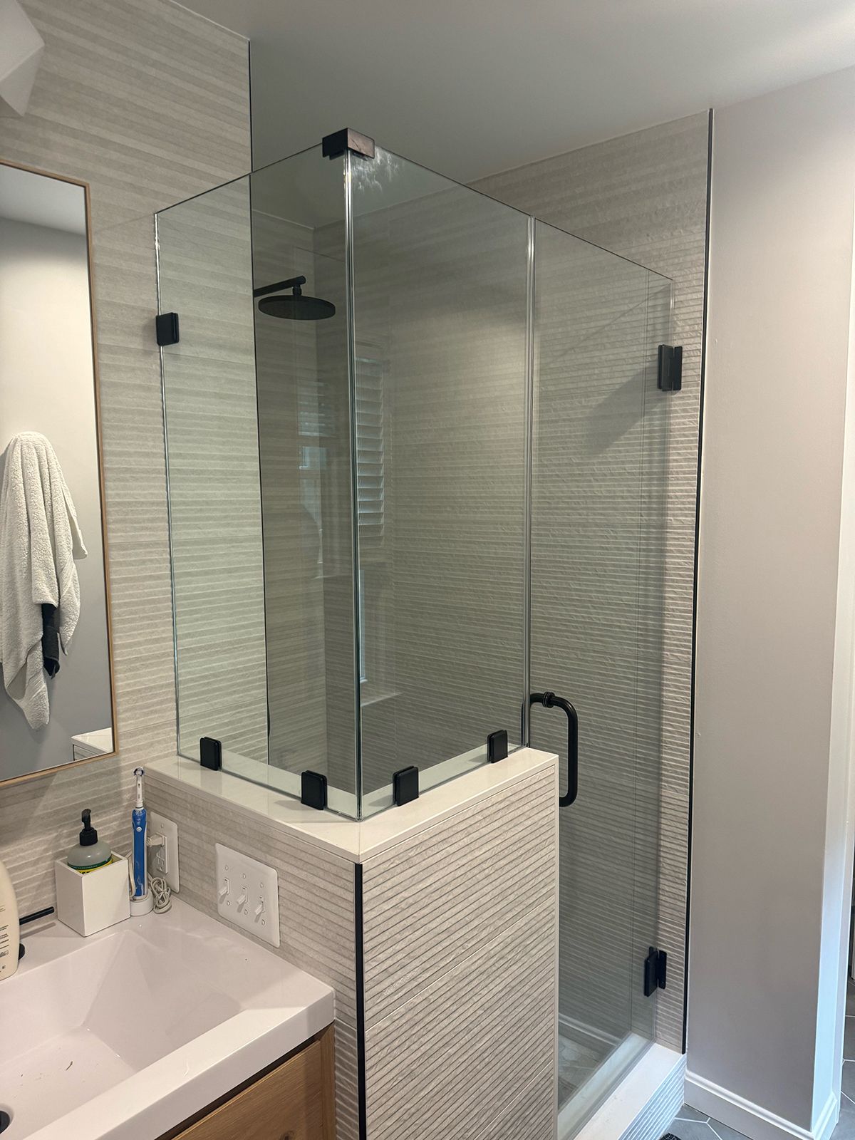 A bathroom with a modern glass shower enclosure featuring black hardware, situated next to a vanity sink and tiled walls.