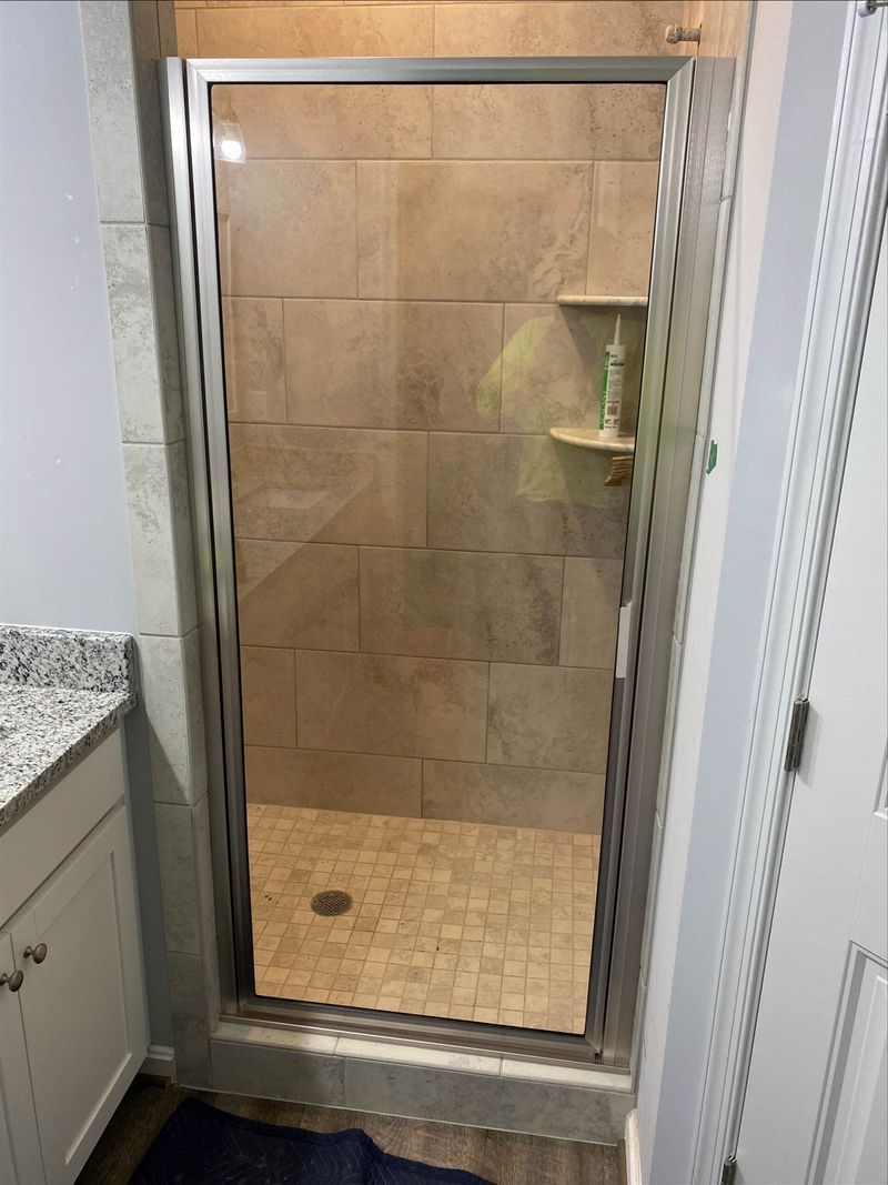 Shower with beige tile walls, glass door, and stone floor.  A small shelf is visible inside.