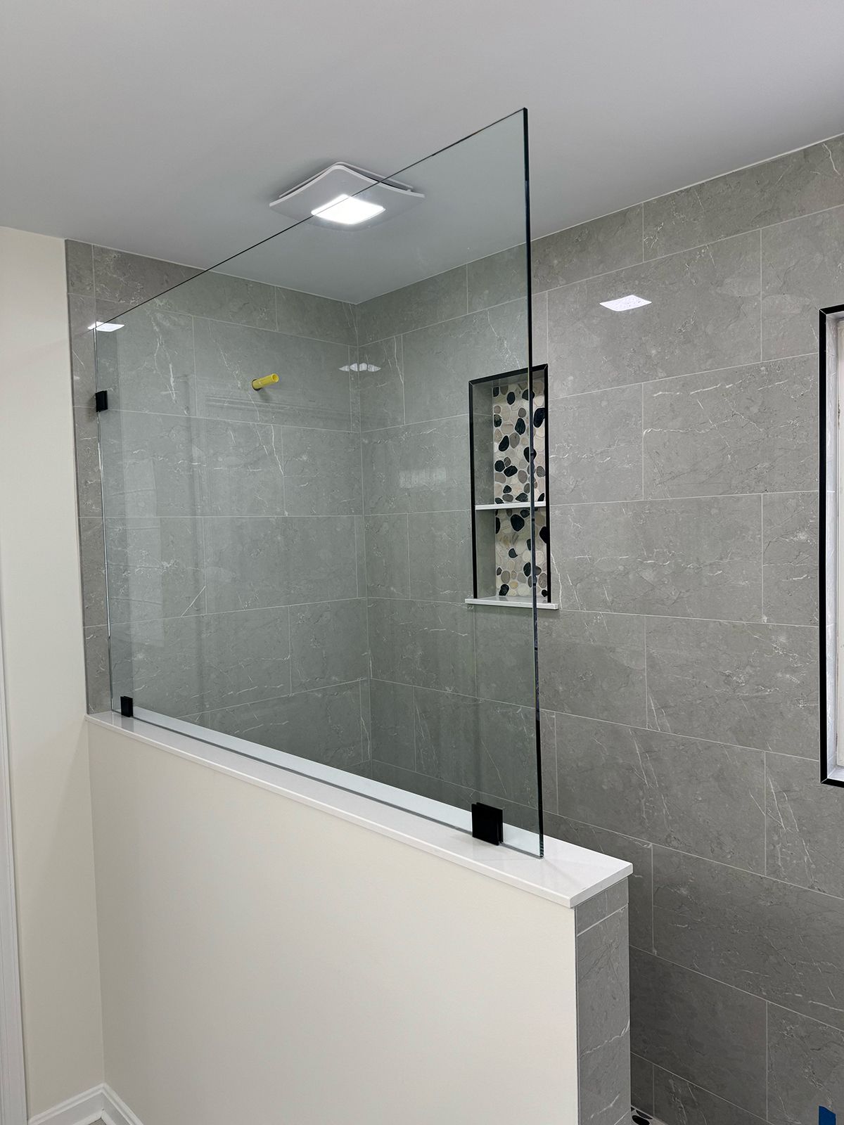 A modern bathroom shower with grey tiled walls, a decorative recessed niche, and a frameless glass partition on a half-wall.