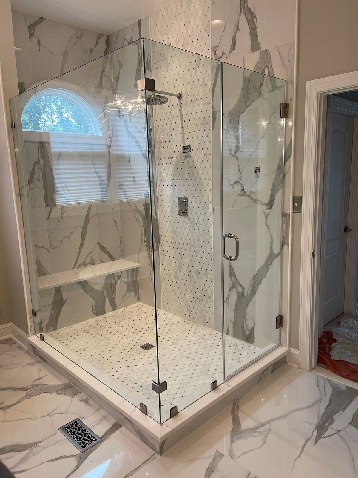 A walk-in shower with white and gray marble tiles, glass doors, a built-in bench, and a modern shower head.
