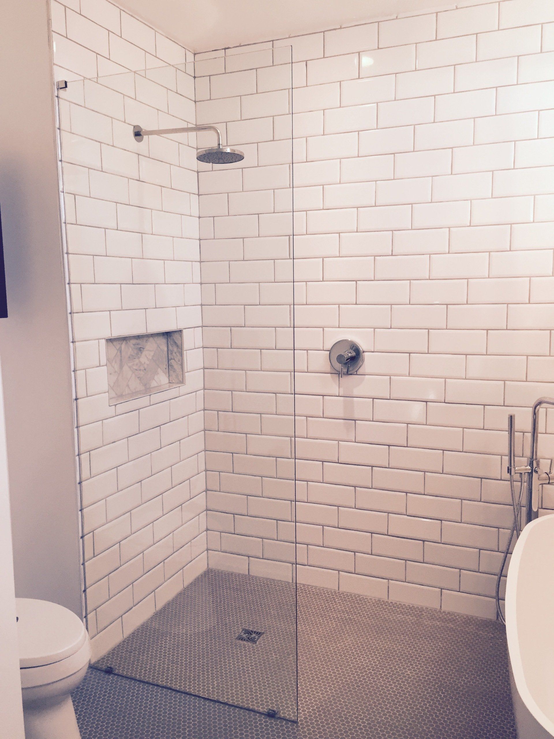 White-tiled shower with a glass door, a rain showerhead, and a recessed shelf.