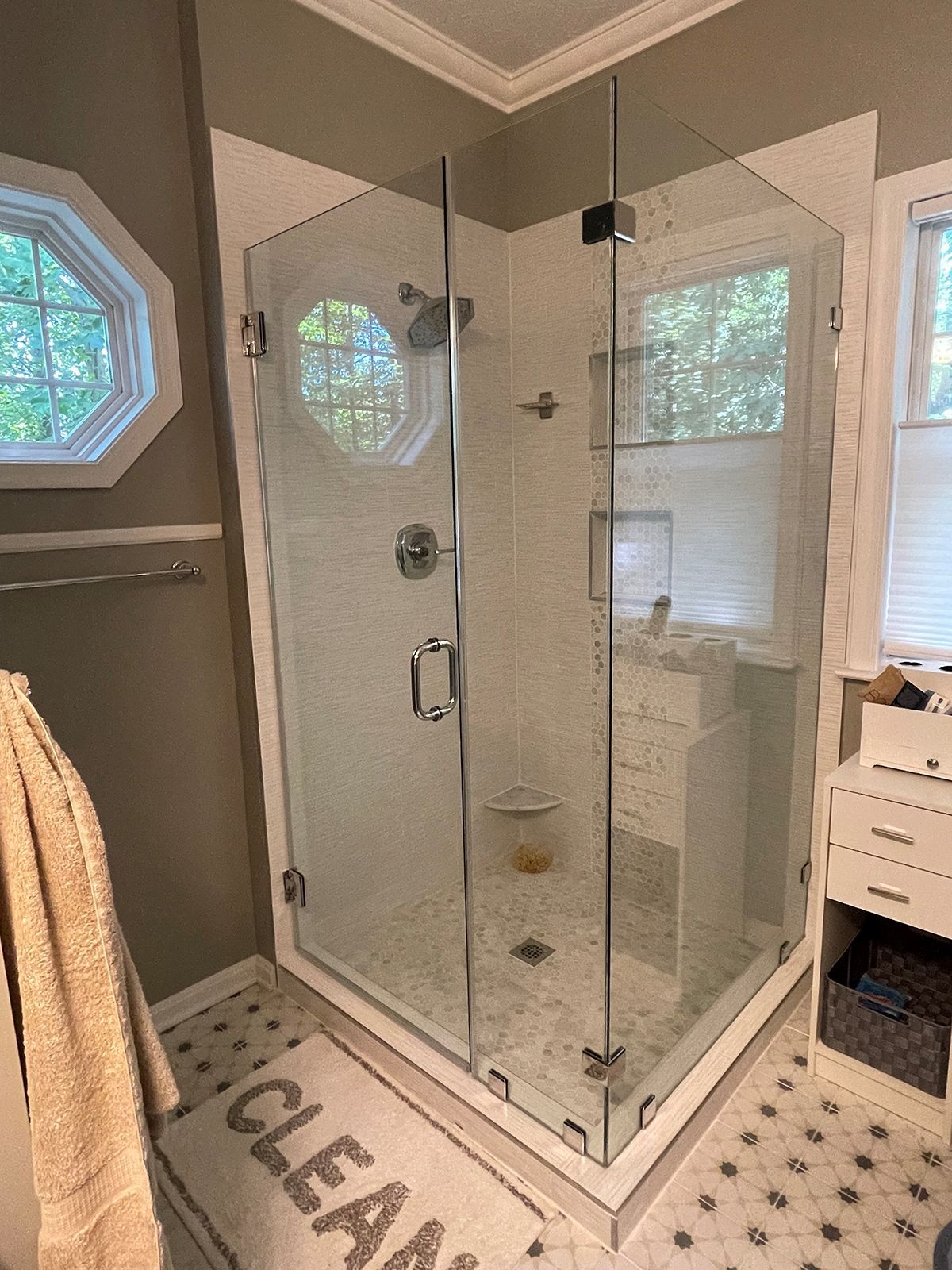 A glass-enclosed shower with white tiled walls and floor in a bathroom with dark walls and a patterned tile floor.