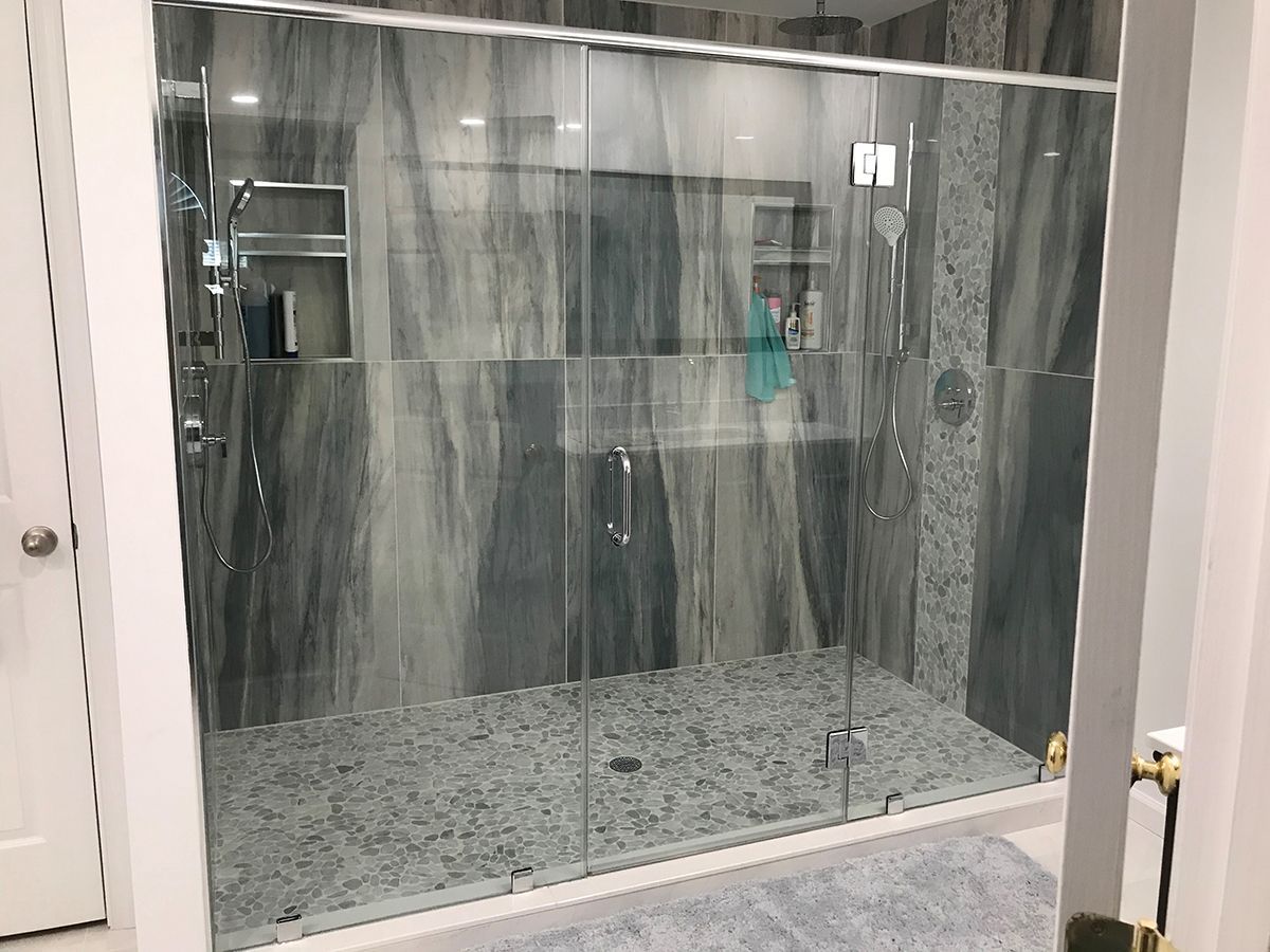 A modern walk-in shower with large grey marble-look tiles, a pebble floor, and a glass enclosure in a bathroom.