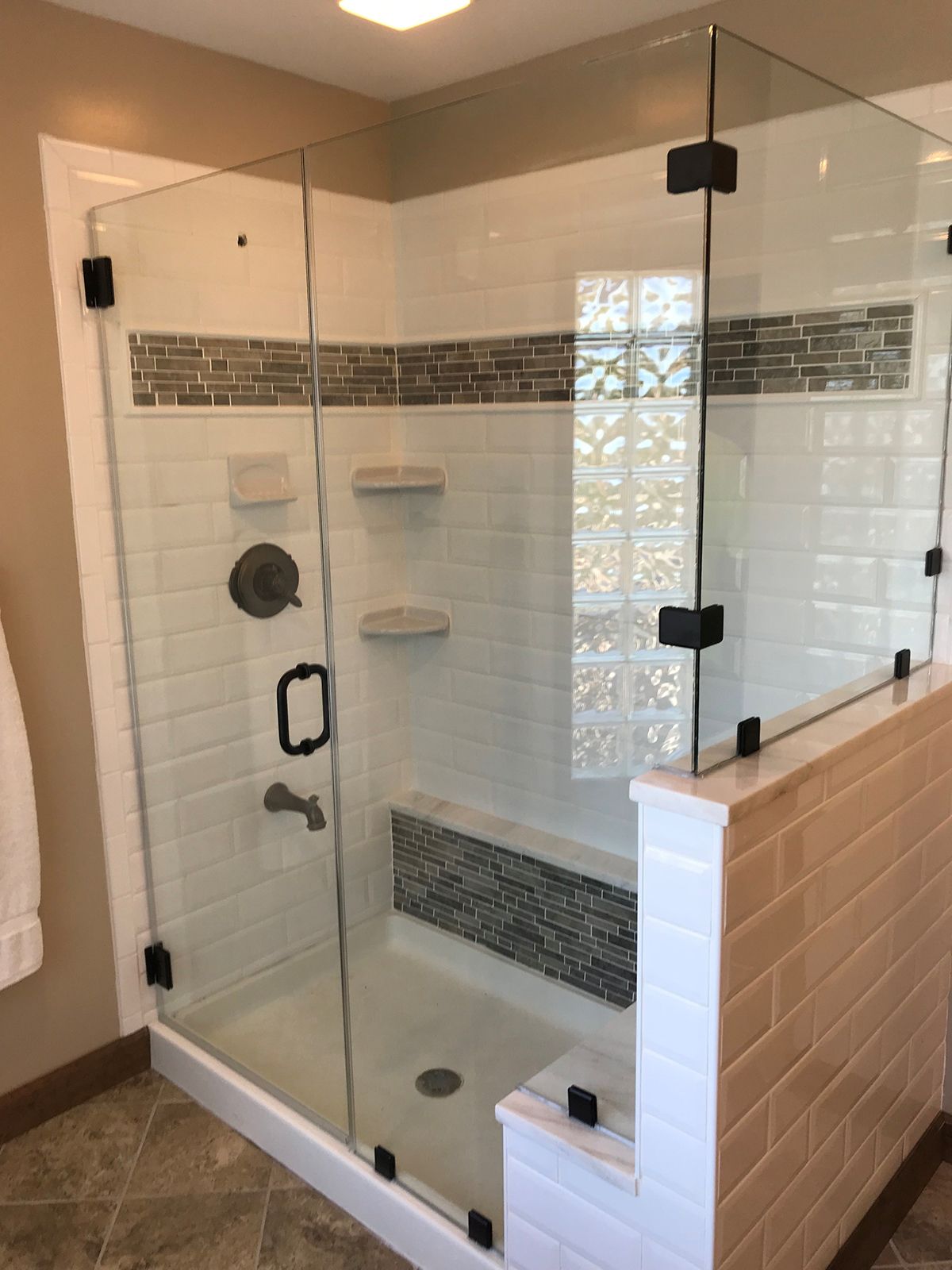 A modern glass-enclosed shower with white subway tiles, dark grey accent trim, a built-in bench, and black hardware.